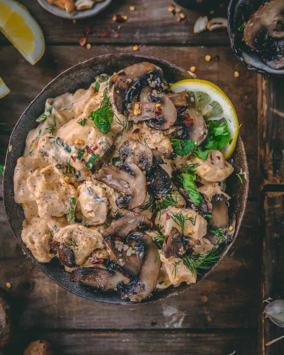 A photo of a bowl of cheesy tortellini with garlicky mushrooms on top